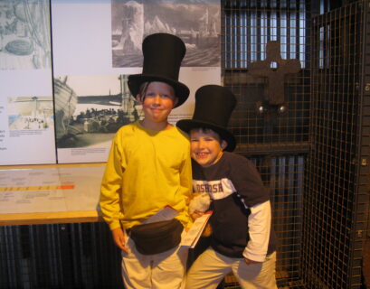 Two children wearing top hats, smiling indoors.