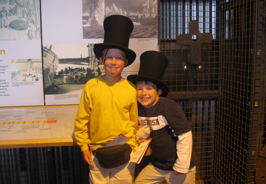 Two children wearing top hats, smiling indoors.