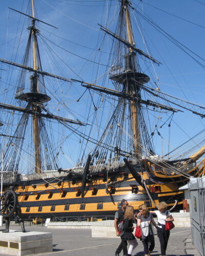 Historic warship docked with visitors nearby.