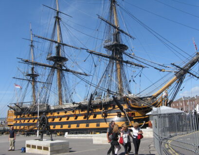 Historic warship docked with visitors nearby.