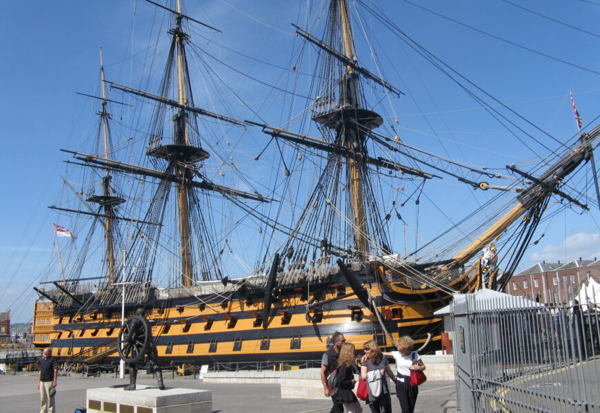 Historic warship docked with visitors nearby.