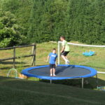 Two kids jumping on a backyard trampoline.
